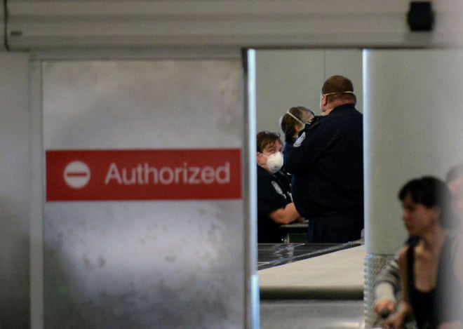 Masked customs officers look on in a screening area for international passengers from United flight 998 from Brussels at Newark airport in Newark, N.J., Saturday, Oct. 4, 2014. New Jersey health officials say Ebola has been ruled out as the cause of illness for a man who became sick on a flight from Brussels to the United States.